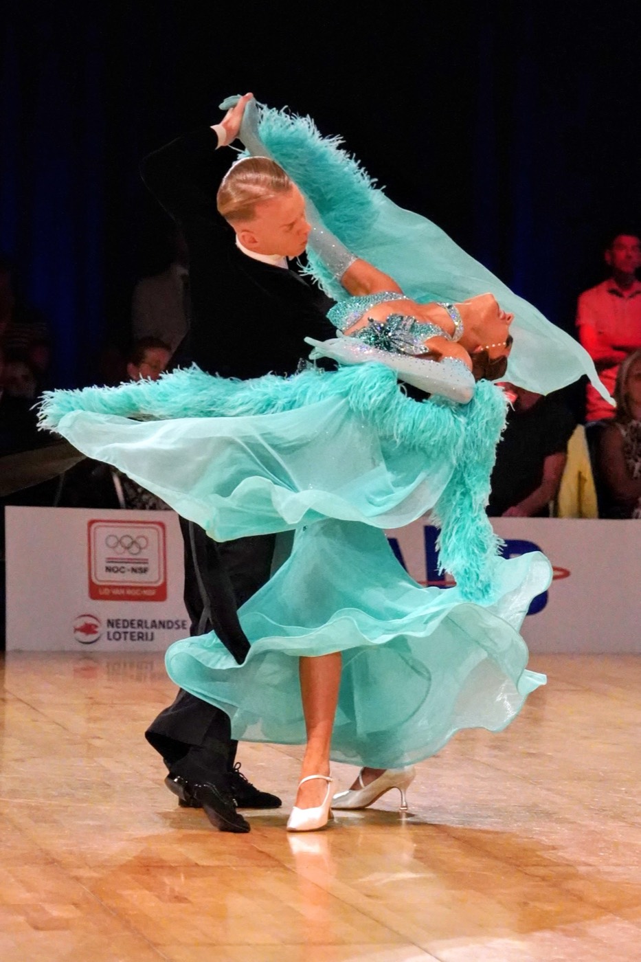 Ballroompaar in turquoise jurk tijdens een wedstrijd